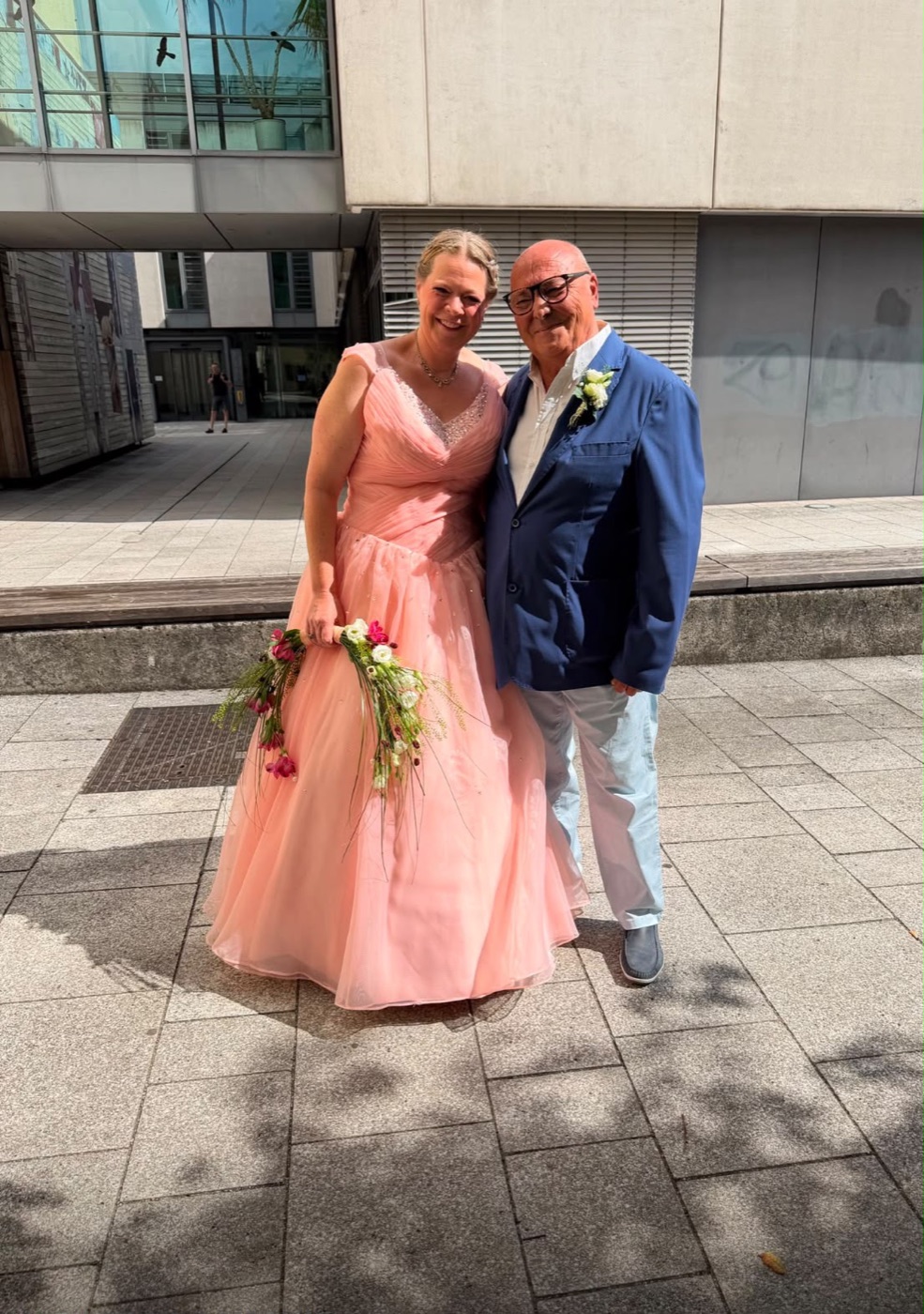 Catrin im pfirsichfarbenen Kleid mit Brautstrauß, Pippo im dunkelblauen Sakko, am Tag der Hochzeit.